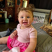 Kaylie joined the competition — help win amazing prizes! baby, child, smiling, pink_dress, blue_eyes, indoor, bed, crib, furniture, curly_hair, cute, happy, person, portrait, toddler, room, blanket, tissue, cozy, hair_buns