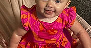 Brynleigh joined the competition — help win amazing prizes! baby, child, smiling, pink_dress, orange_pattern, cushioned_chair, indoor, portrait, happy, cute, person, sitting, infant, playful, face, blue_eyes, short_hair, soft_fabric, home, bright_colors