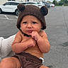 Kohen is registered to the contest to win money with this photo: baby, bear_ears, brown_hat, cars, child, cloudy_day, curious, cute, expression, fist, fuzzy_hat, hat, infant, outdoor, parking_lot, person_holding, portrait, shorts, skin, sweater