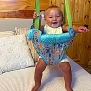 Kohen is registered to the contest to win money with this photo: baby, baby_jumper, bouncer, child, clothing, cute, fabric, furniture, happy, home, indoor, infant, joy, person, pillow, play, room, seat, smiling, wooden_wall