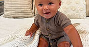 Kohen joined the competition — help win amazing prizes! baby, child, infant, smiling, sitting, blanket, knitted_blanket, pillow, striped_pillow, decorative_pillow, wooden_wall, indoors, cozy, cute, clothing, onesie, happy, face, skin, person