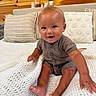 baby, child, infant, smiling, sitting, blanket, knitted_blanket, pillow, striped_pillow, decorative_pillow, wooden_wall, indoors, cozy, cute, clothing, onesie, happy, face, skin, person