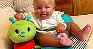 Kohen is registered to the contest to win money with this photo: baby, child, clothing, colorful, cozy, cushion, cute, face, feet, happy, indoor, infant, person, pillow, plush, sitting, smiling, tongue_out, toy, wooden_wall
