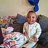 Queen is registered to the contest to win money with this photo: baby, child, smiling, pajamas, couch, pillow, clothing, fabric, indoor, person, happy, cute, seated, home, colorful, blanket, face, portrait, infant, cozy