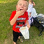 child, boy, popcorn, red_shirt, black_shorts, colorful_shoes, grass, outdoor, toddler, blanket, wagon, cooler, drink_bottle, playing, summer, snack, happy, casual_clothing, nature, daylight