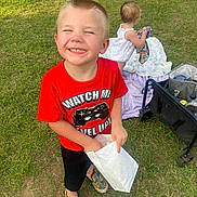 Frankie is registered to the contest to win money with this photo: black_shorts, blanket, boy, child, colorful_shoes, daytime, family, fun, grass, happy, outdoor, park, playing, popcorn, red_shirt, smile, summer, toddler, toy, wagon