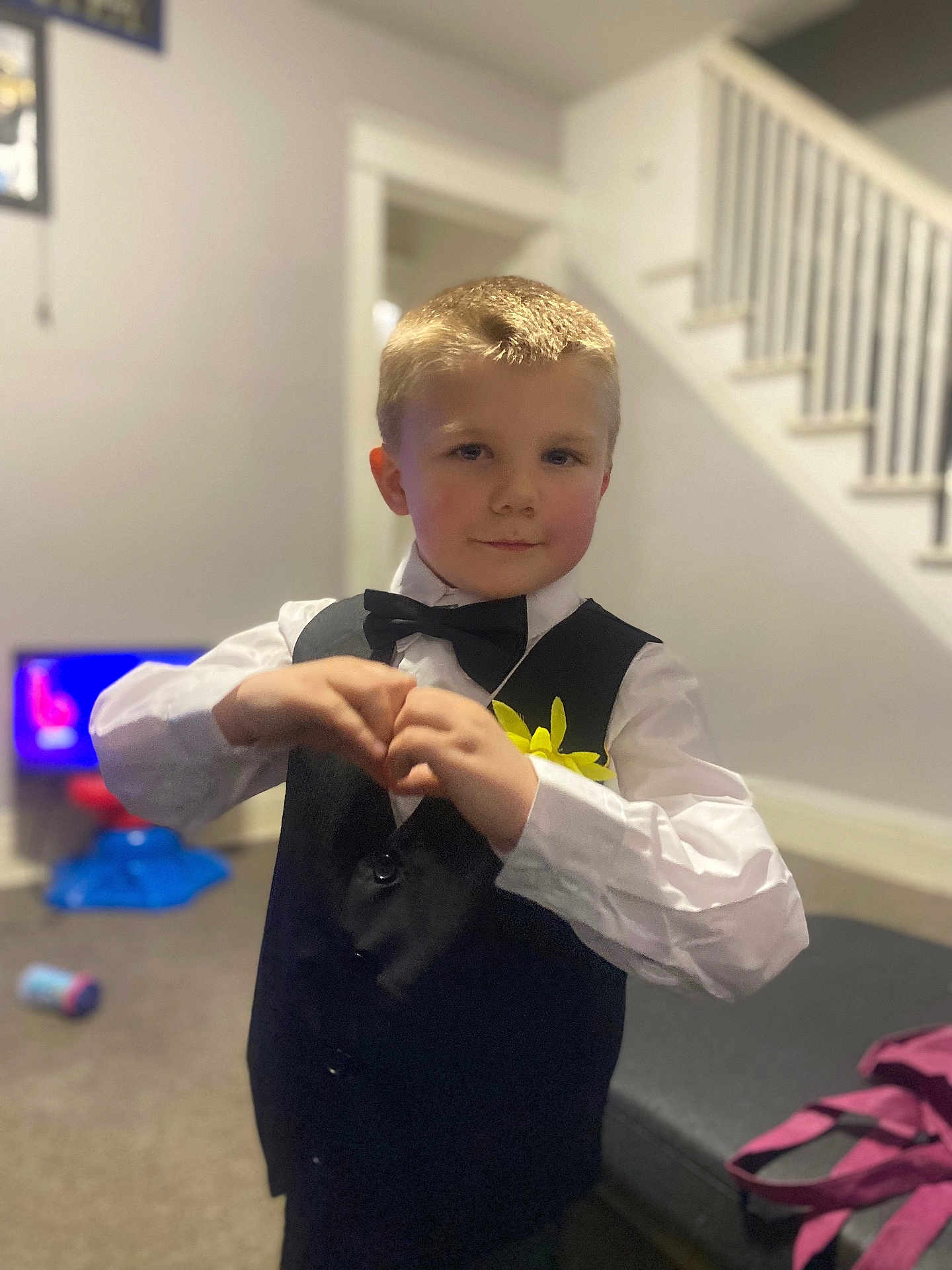 Frankie joined the competition — help win amazing prizes! child, boy, indoor, vest, bow_tie, white_shirt, heart_hands, smile, blond_hair, carpet, stairs, toy, living_room, casual, portrait, person, cute, home, yellow_flower, furniture