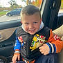Frankie is registered to the contest to win money with this photo: child, boy, smiling, car, jacket, mario, bowser, seatbelt, window, autumn, trees, parked_car, casual_clothing, indoor, portrait, happy, young_child, colorful_clothing, seat, daytime