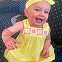 baby, child, yellow_dress, headband, smiling, indoor, couch, blue_couch, patterned_fabric, cute, happy, portrait, sitting, infant, toddler, person, clothing, face, hand, bright_colors