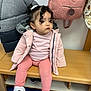 child, toddler, pink_jacket, curly_hair, bench, indoor, shoes, coat, backpack, wooden_furniture, floor, casual_clothing, young_child, curly_hair_bangs, white_shoes, pink_pants, sitting, person, cute, portrait