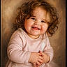toddler, child, smiling, curly_hair, portrait, pink_clothing, baby, happy, hands, face, cute, studio, warm_background, sitting, innocent, young_child, skin, expression, photography, closeup