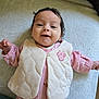 apparel, baby, blanket, casual, child, cozy, cute, face, happy, indoors, infant, lying_down, person, pink_clothing, portrait, smiling, soft_texture, vest, warm_clothing, young_child