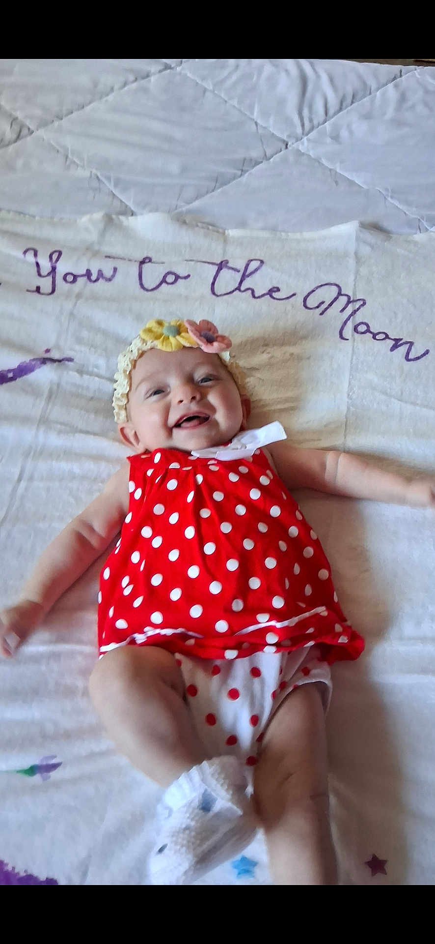 Olivia is registered to the contest to win money with this photo: baby, infant, smiling, red_dress, polka_dots, headband, flower, blanket, lying_down, white_blanket, happy, cute, child, person, footwear, sock, indoors, celebration, joy, adorable
