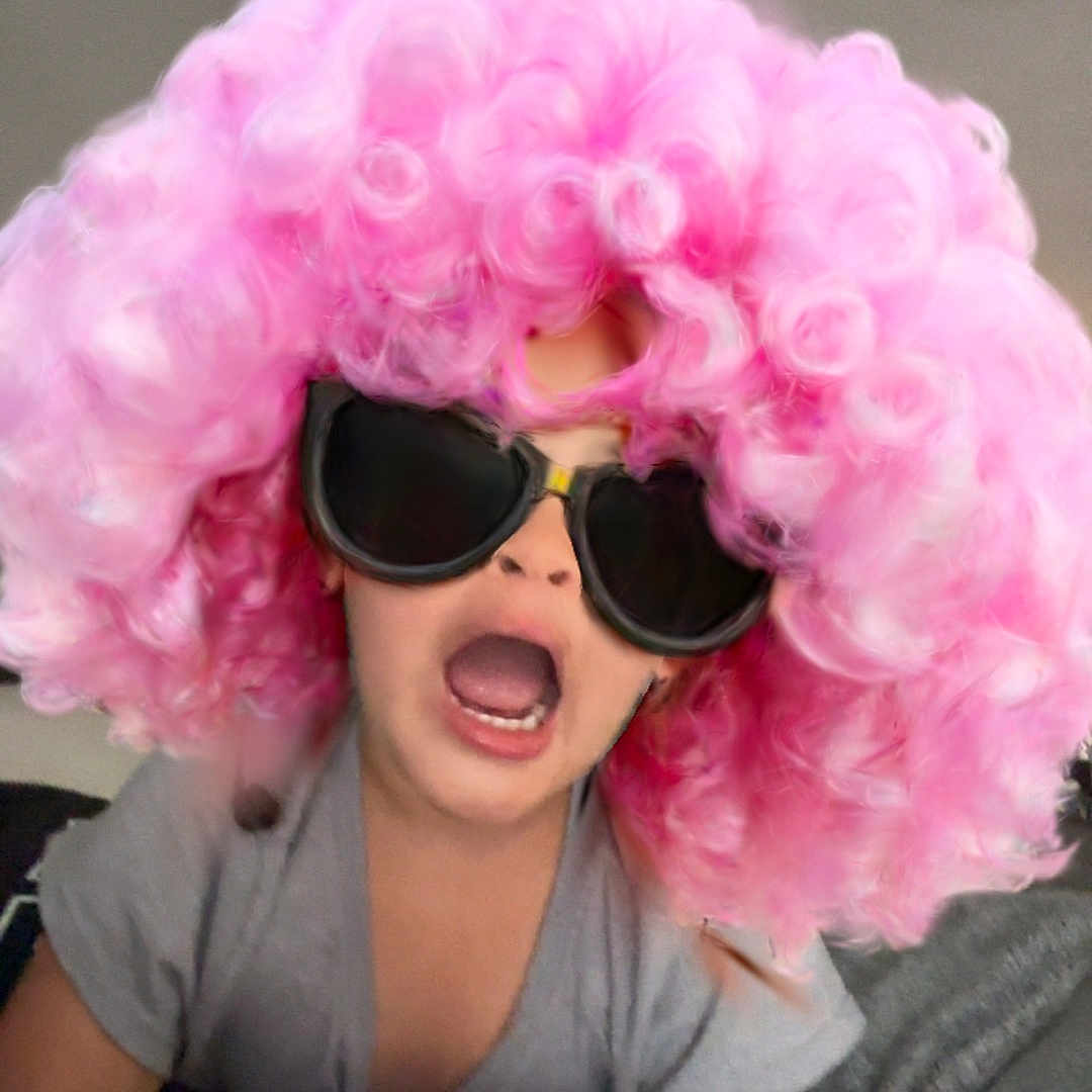 Demi is registered to the contest to win money with this photo: child, pink_wig, sunglasses, funny_face, playful, indoor, curly_hair, costume, expression, tshirt, person, portrait, humor, fashion, cute, childhood, casual, home, entertainment, colorful