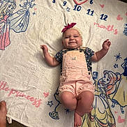 Jacqueline is registered to the contest to win money with this photo: baby, girl, smiling, blanket, princess, overalls, headband, bow, numbers, months, cartoon, character, lying_down, happy, cute, indoor, carpet, feet, child, portrait