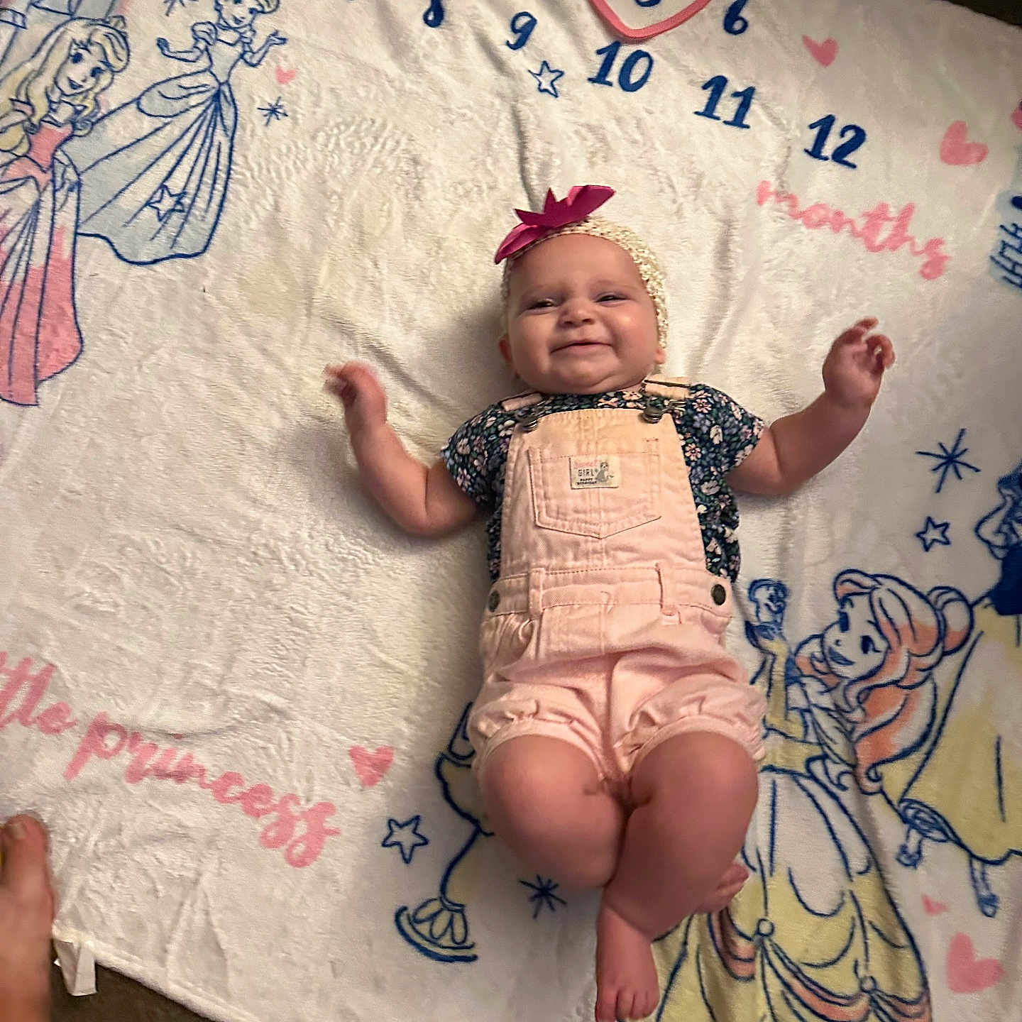 Jacqueline is registered to the contest to win money with this photo: baby, blanket, bow, carpet, cartoon, character, child, cute, feet, girl, happy, headband, indoor, lying_down, months, numbers, overalls, portrait, princess, smiling