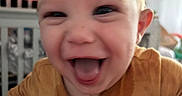 Brady is registered to the contest to win money with this photo: baby, blurred_background, child, closeup, crib, cute, expression, face, happy, head, home, indoor, infant, joy, mouth_open, mustard_outfit, person, smiling, tongue_out, young_child