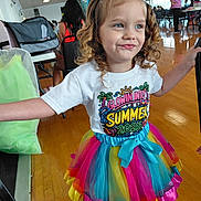 Delilah joined the competition — help win amazing prizes! child, girl, curly_hair, blue_bow, rainbow_tutu, white_tshirt, indoor, wooden_floor, people, background, colorful_clothing, smiling, pose, event, party, fashion, happy, young, cute, celebration