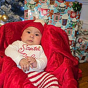 Hadassa is registered to the contest to win money with this photo: baby, child, christmas, holiday, red_hat, red_blanket, white_sweater, striped_pants, gift_wrap, christmas_tree, ornaments, present, festive, indoors, couch, holiday_decor, cute, portrait, smiling, warm