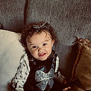 Amaya joined the competition — help win amazing prizes! toddler, child, curly_hair, bow, black_outfit, sparkly_bow, couch, pillows, white_shirt, smile, indoor, portrait, person, cute, happy, sitting, playful, young_child, cozy, home
