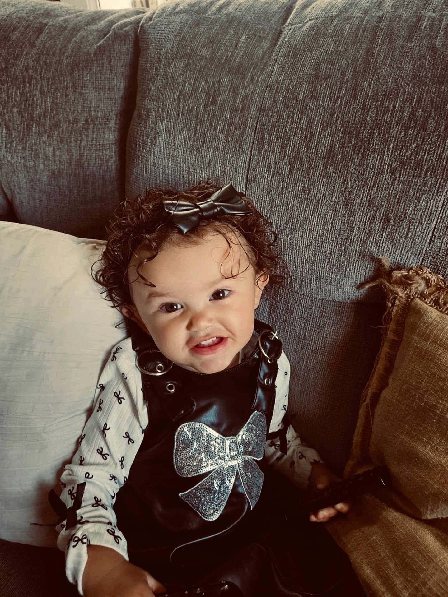 Amaya joined the competition — help win amazing prizes! toddler, child, curly_hair, bow, black_outfit, sparkly_bow, couch, pillows, white_shirt, smile, indoor, portrait, person, cute, happy, sitting, playful, young_child, cozy, home