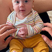Jasper is registered to the contest to win money with this photo: baby, infant, child, person, clothing, striped_shirt, yellow_pants, hands, feet, couch, cushion, indoor, sitting, looking_at_camera, cute, human, skin, legs, head, eyes