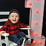 toddler, child, smile, happy, rocking_chair, white_chair, number_one, red_lights, cap, black_cap, checkered_shirt, red_shirt, jeans, sneakers, footwear, indoor, celebration, portrait, excited, playful