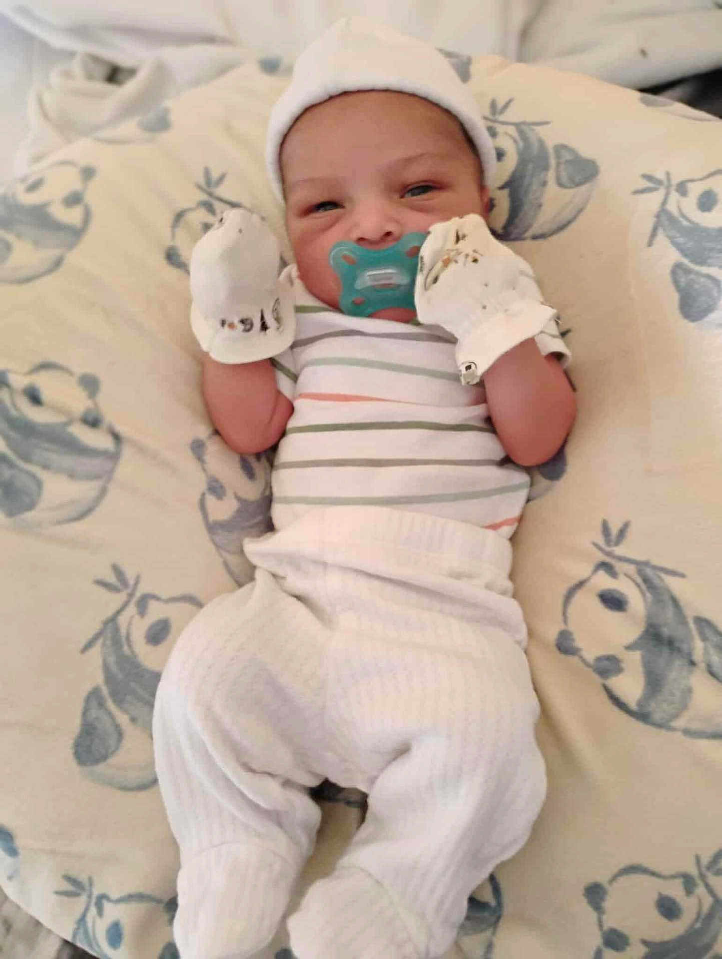 Karson Cain is registered to the contest to win money with this photo: baby, newborn, pacifier, mittens, hat, striped_shirt, blanket, infant, sleepy, clothing, lying_down, cute, soft, cute_baby, pattern, white_pants, small_hands, resting, portrait, indoors