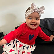 Esmée participe au concours pour gagner de l'argent avec cette photo : baby, toddler, headband, bow, smile, tongue_out, red_sweater, heart_skirt, skirt, sitting, sofa, black_sofa, indoor, white_wall, happy, face, eyes, hand, portrait, clothing