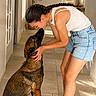 Aka a rejoint le concours — aidez-le/la à gagner de superbes lots ! woman, dog, german_shepherd, indoor, floor, tile_floor, casual_clothing, braided_hair, glasses, shorts, tank_top, slippers, pet, affection, interaction, hallway, plant, door, vase, natural_light