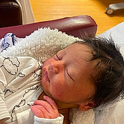 Sheldon is registered to the contest to win money with this photo: newborn, baby, sleeping, blanket, white_clothing, hand, face, hair, indoor, furniture, chair, wood_floor, cozy, peaceful, infant, portrait, soft_texture, closeup, rest, relaxation