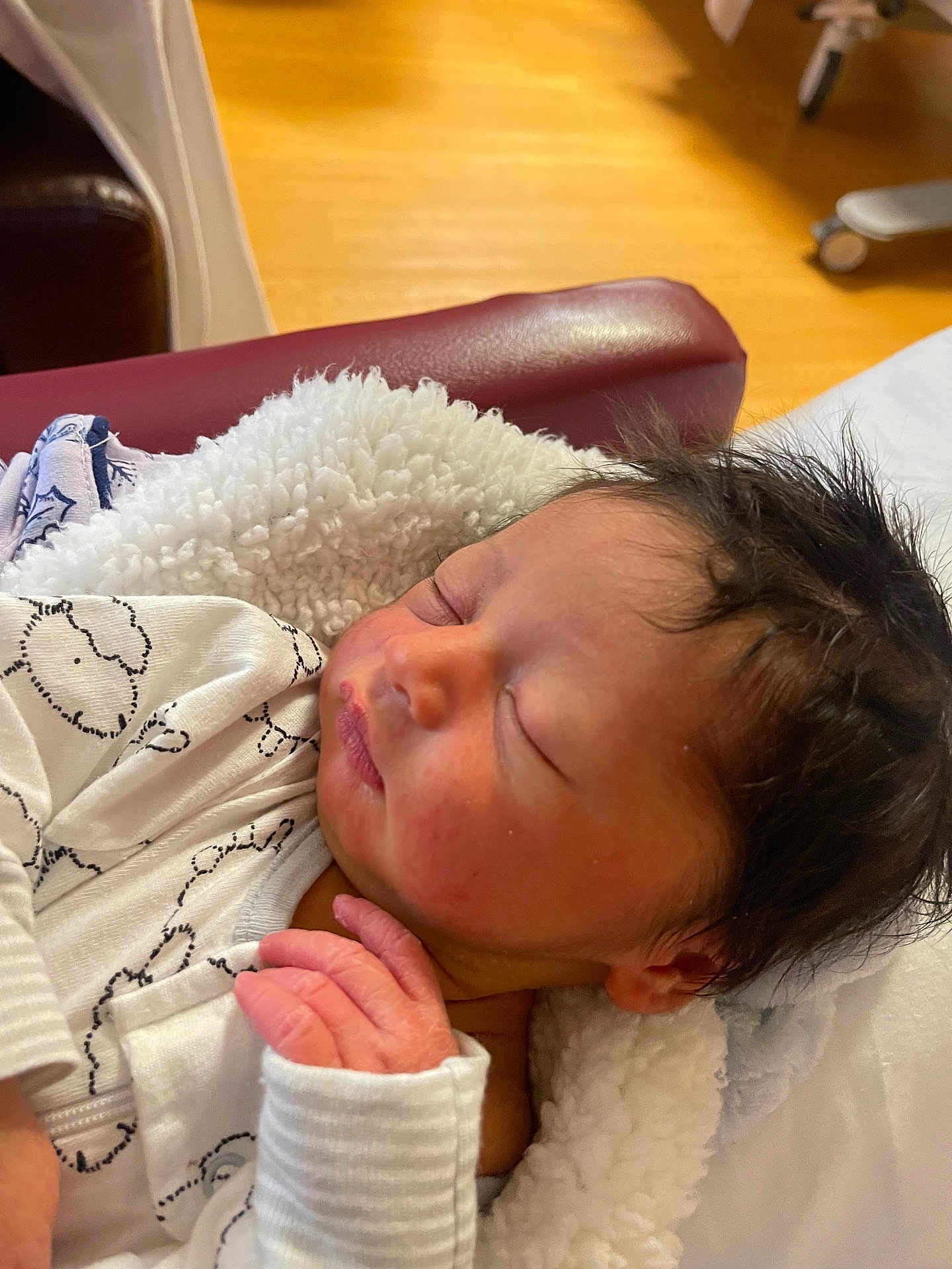Sheldon is registered to the contest to win money with this photo: newborn, baby, sleeping, blanket, white_clothing, hand, face, hair, indoor, furniture, chair, wood_floor, cozy, peaceful, infant, portrait, soft_texture, closeup, rest, relaxation