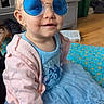 toddler, child, baby, glasses, blue_sunglasses, pink_jacket, blue_dress, sitting, indoor, blanket, floor, dresser, smiling, cute, person, fashion, portrait, home, clothing, footwear