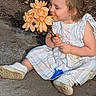 toddler, child, flower, outdoor, garden, smile, dress, shoes, plant, nature, sitting, cute, happy, person, young_child, blossom, sunlight, daytime, curly_hair, holding