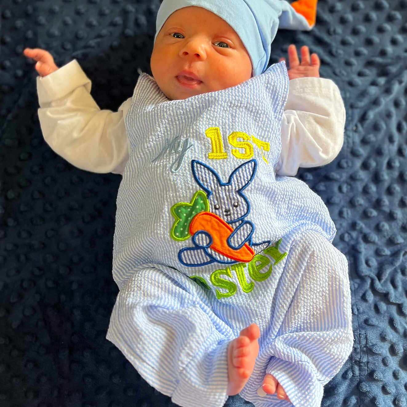 Elijah is registered to the contest to win money with this photo: applique, baby, blanket, bodypart, bonnet, cap, clothing, embroidery, face, finger, hand, hat, head, newborn, pants, pattern, person, photography, portrait, sleeve