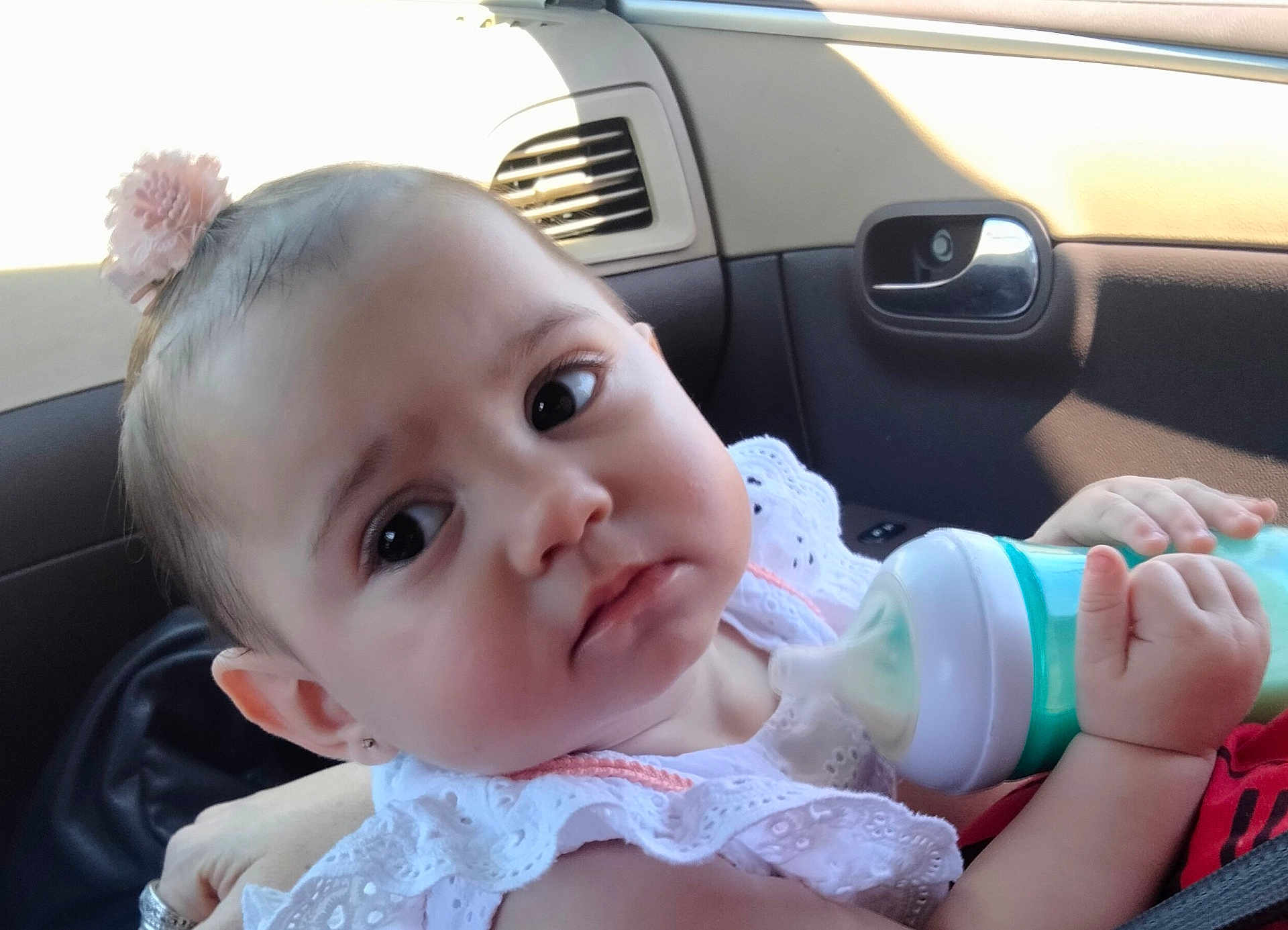 Angelina joined the competition — help win amazing prizes! baby, child, bottle, car_interior, white_clothing, pink_hair_accessory, face, hand, infant, portrait, seatbelt, window, door_handle, curious, young_child, cute, skin, eyes, sitting, feeding