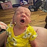 baby, infant, child, yawning, sleepy, yellow_outfit, floral_clothing, sitting, portrait, close_up, indoor, home, family_room, television, baby_gear, toys, shelves, wood_floor, caregiver, funny_expression