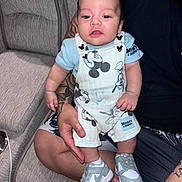 Tatum is registered to the contest to win money with this photo: arm, baby, casual, child, clothing, couch, cute, face, footwear, hand, happy, indoor, infant, mickey_mouse, overalls, person, seated, smiling, sneakers, tattoo