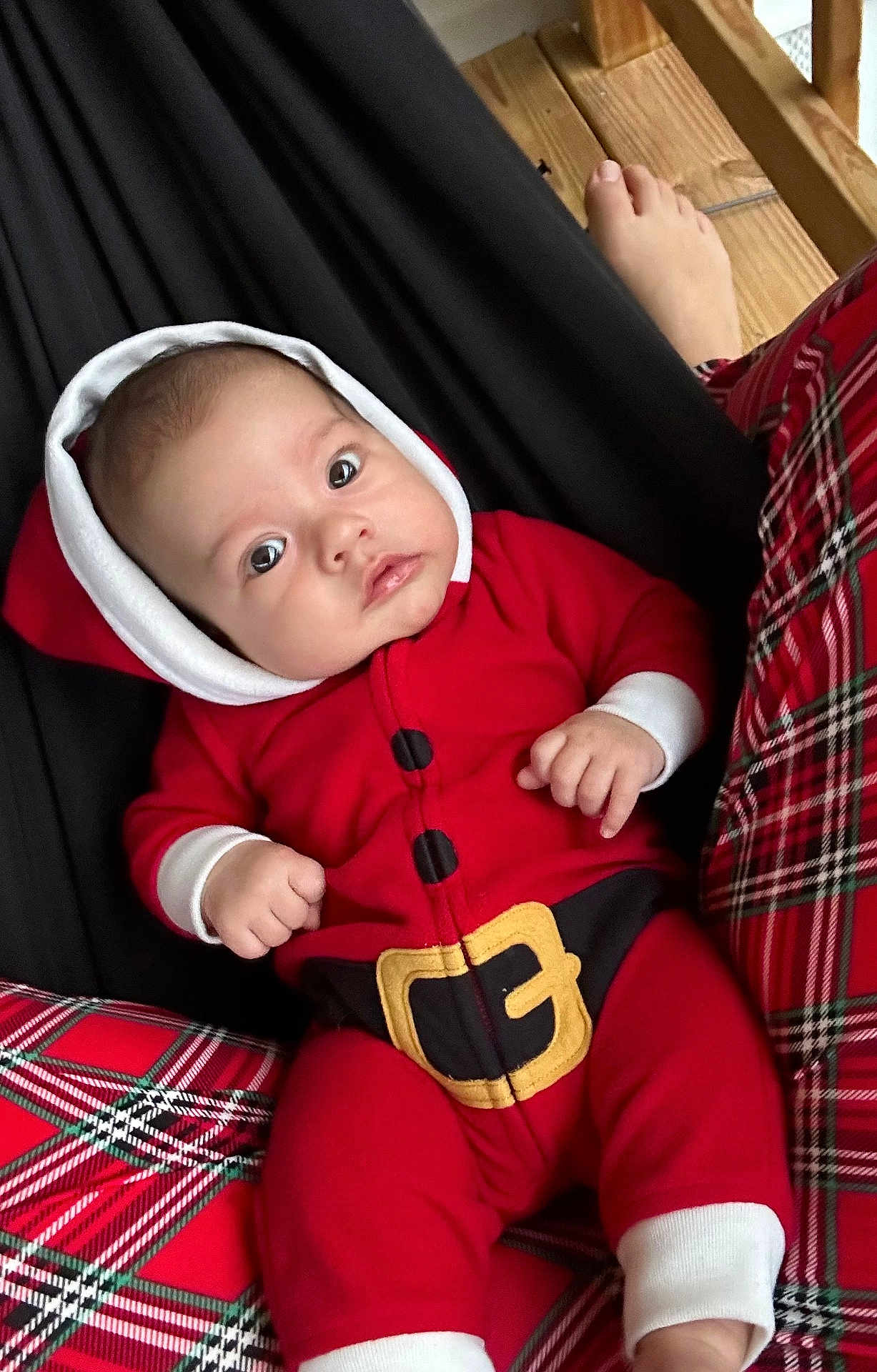 Tatum joined the competition — help win amazing prizes! baby, infant, red_clothing, hooded_onesie, plaid, pattern, foot, wood, fabric, cozy, holiday, festive, cute, portrait, indoors, relaxed, person, child, sitting, closeup