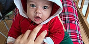 Tatum is registered to the contest to win money with this photo: baby, casual, child, closeup, cozy, cute, expression, face, hand, hood, indoor, infant, legs, person, plaid, playful, porch, red_clothing, sitting, wood
