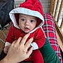 Tatum is registered to the contest to win money with this photo: baby, child, hood, red_clothing, hand, plaid, legs, porch, wood, expression, face, person, sitting, cute, infant, cozy, casual, indoor, closeup, playful