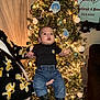 Tatum is registered to the contest to win money with this photo: baby, child, christmas_tree, holiday_decor, ornaments, lights, jeans, boots, black_shirt, person_holding, indoor, festive, celebration, living_room, decorations, happy, cute, winter_clothing, family, holiday
