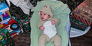 Tatum is registered to the contest to win money with this photo: baby, infant, christmas_tree, christmas_lights, presents, gift_wrap, holiday, onesie, baby_chair, flooring, wood_floor, decorations, pine_cones, ornaments, green_blanket, socks, indoors, festive, child, cozy