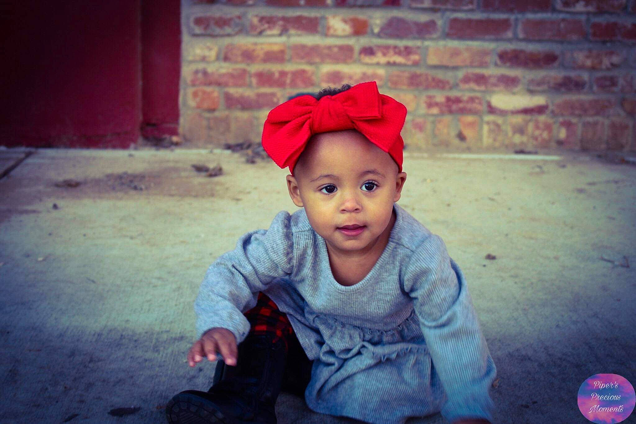 Laina is registered to the contest to win money with this photo: baby, baby_toddler_clothing, bonnet, brick, brickwork, cheek, child, child_model, costume_accessory, headband, headgear, maroon, person, photo_shoot, pink, portrait_photography, red, toddler