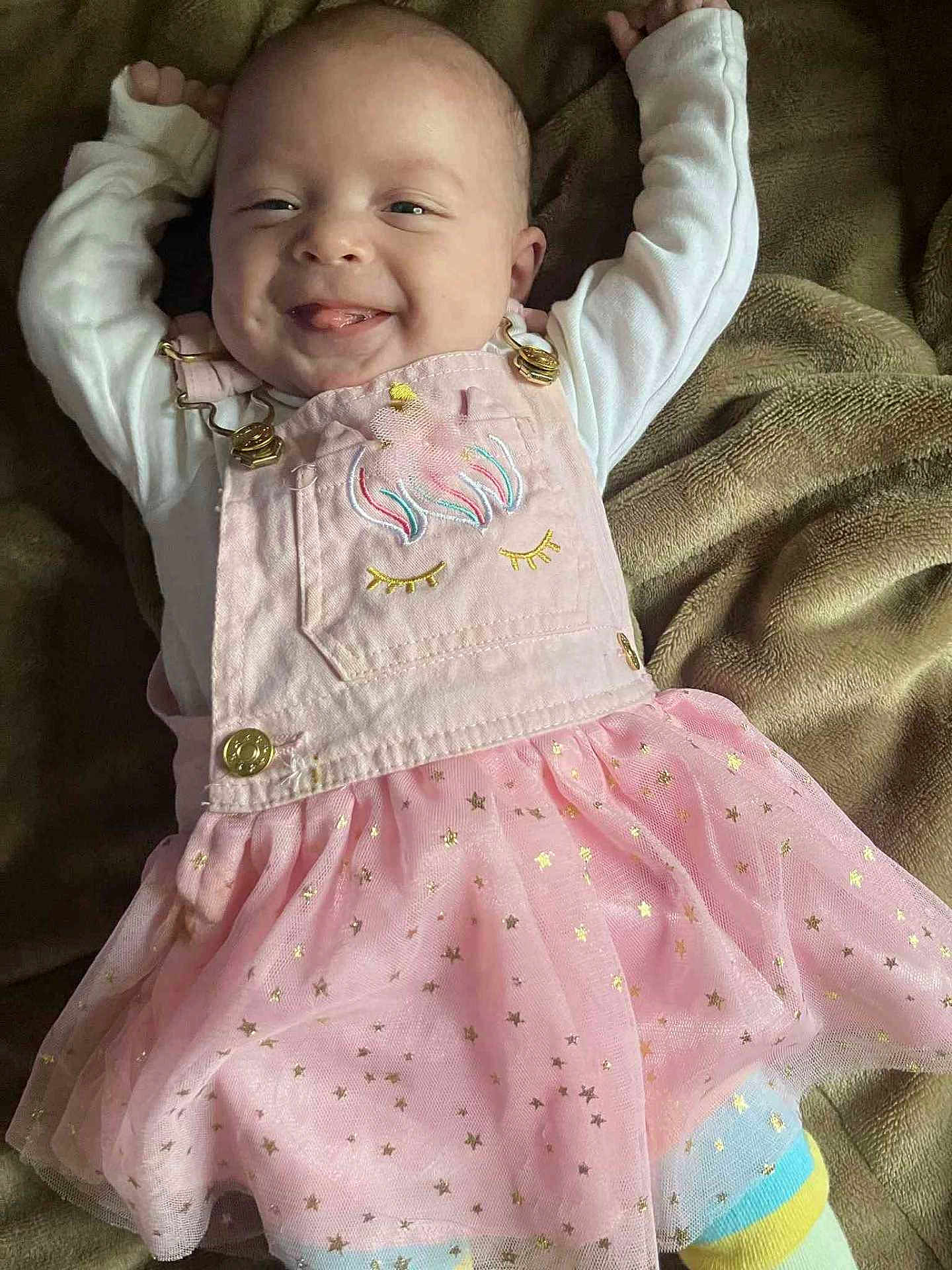 Kadence is registered to the contest to win money with this photo: baby, child, smiling, pink_dress, tutu, star_pattern, long_sleeve_shirt, blanket, happy, tongue_out, cute, infant, face, person, lying_down, cozy, soft, golden_buttons, head, playful