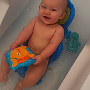 Jules a rejoint le concours — aidez-le/la à gagner de superbes lots ! baby, bath_seat, bath_time, bathtub, blue, child, face, fish_toy, happy, head, indoors, orange, person, playing, skin, smiling, splashing, toy, water, water_toy
