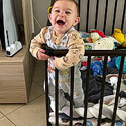 Raphaël participe au concours pour gagner de l'argent avec cette photo : baby, child, playpen, toys, smiling, happy, indoor, furniture, floor, cushion, clothing, person, standing, railing, head, face, room, wood, blanket, toddler