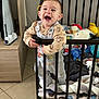 baby, child, playpen, toys, smiling, happy, indoor, furniture, floor, cushion, clothing, person, standing, railing, head, face, room, wood, blanket, toddler