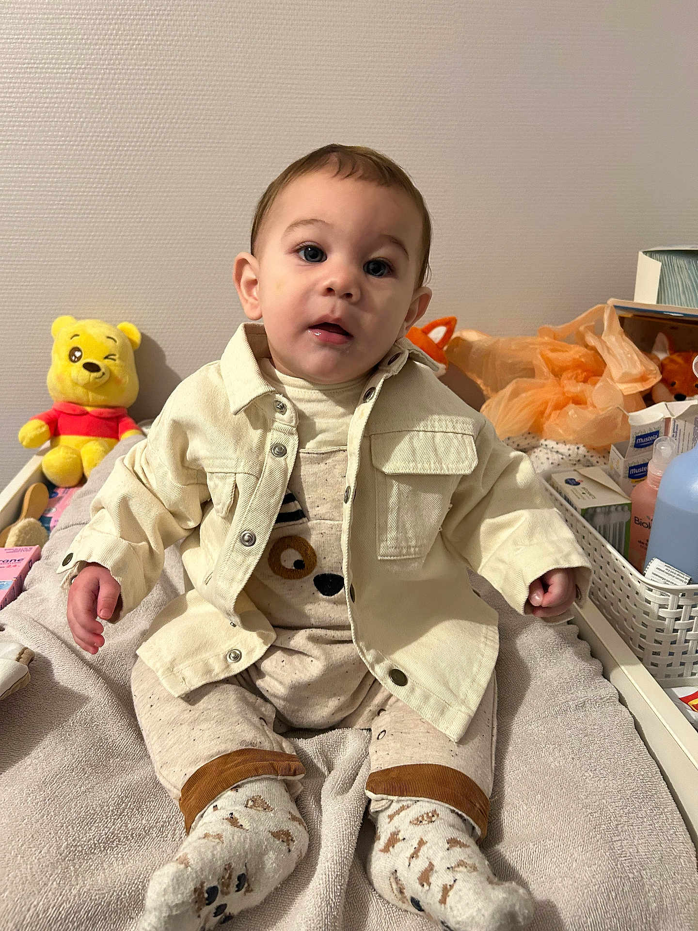 Raphaël a rejoint le concours — aidez-le/la à gagner de superbes lots ! toddler, baby, child, face, clothing, socks, plush_toy, winnie_the_pooh, bed, blanket, toy, basket, bottle, container, indoor, person, sitting, curious, soft_texture, home