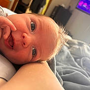 Beau is registered to the contest to win money with this photo: baby, close_up, face, smile, hand, arm, blanket, indoor, cozy, infant, skin, person, newborn, cute, child, portrait, resting, soft_light, warm, happy